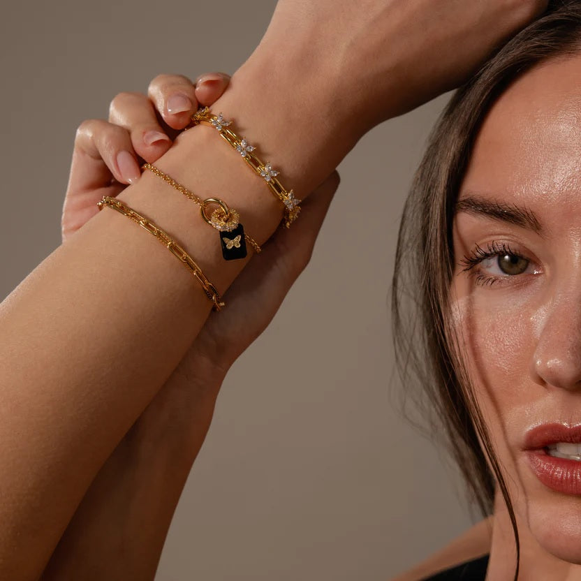 Close-up of a woman's arm wearing multiple gold bracelets with a neutral background