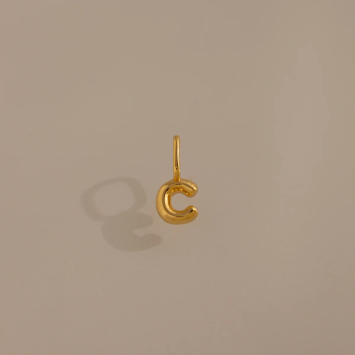 Gold 'C' shaped pendant on a beige background