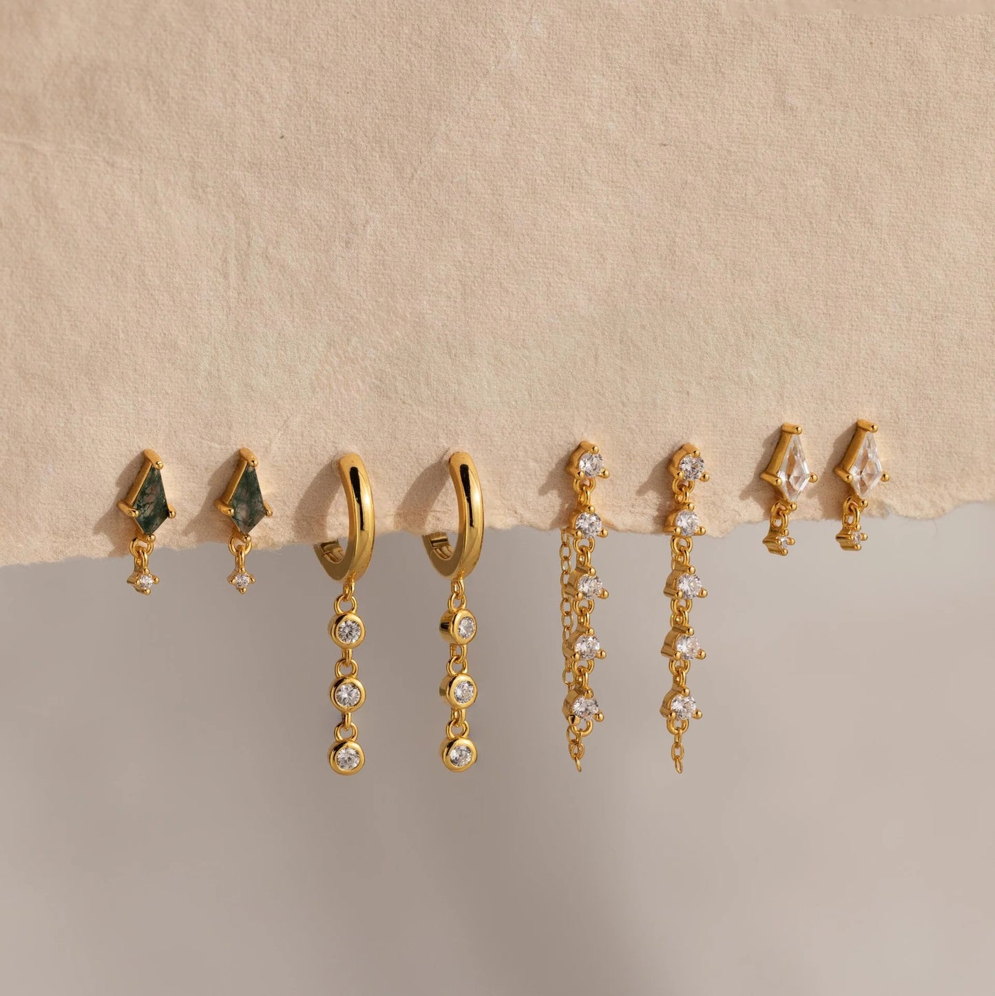 Set of gold and gemstone earrings on a beige background