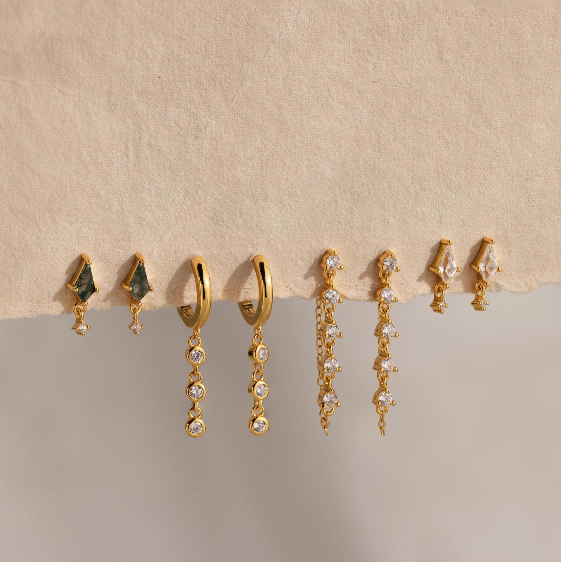 Set of gold and gemstone earrings on a beige background