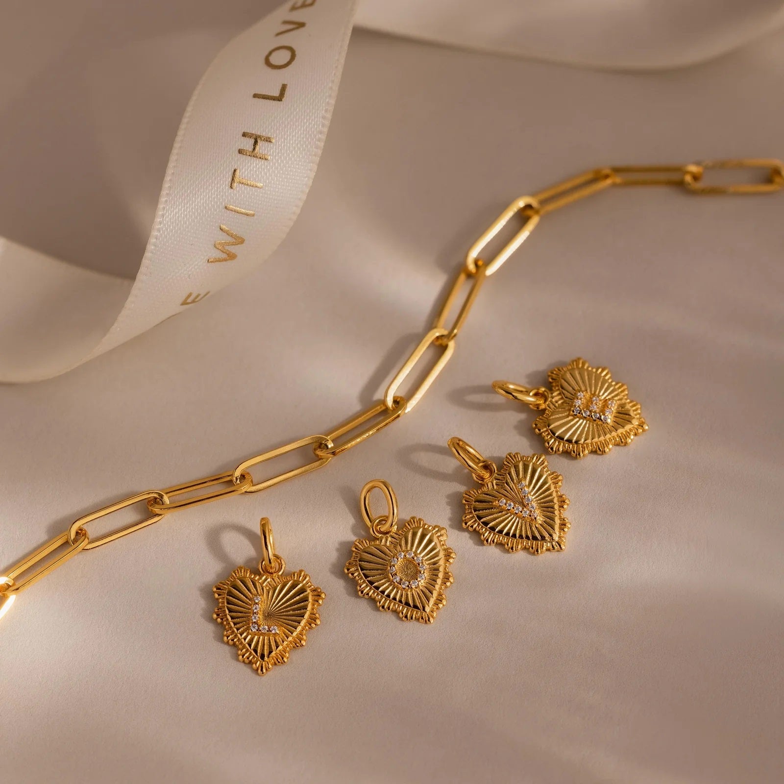 Gold chain necklace with heart-shaped pendants on a beige surface.