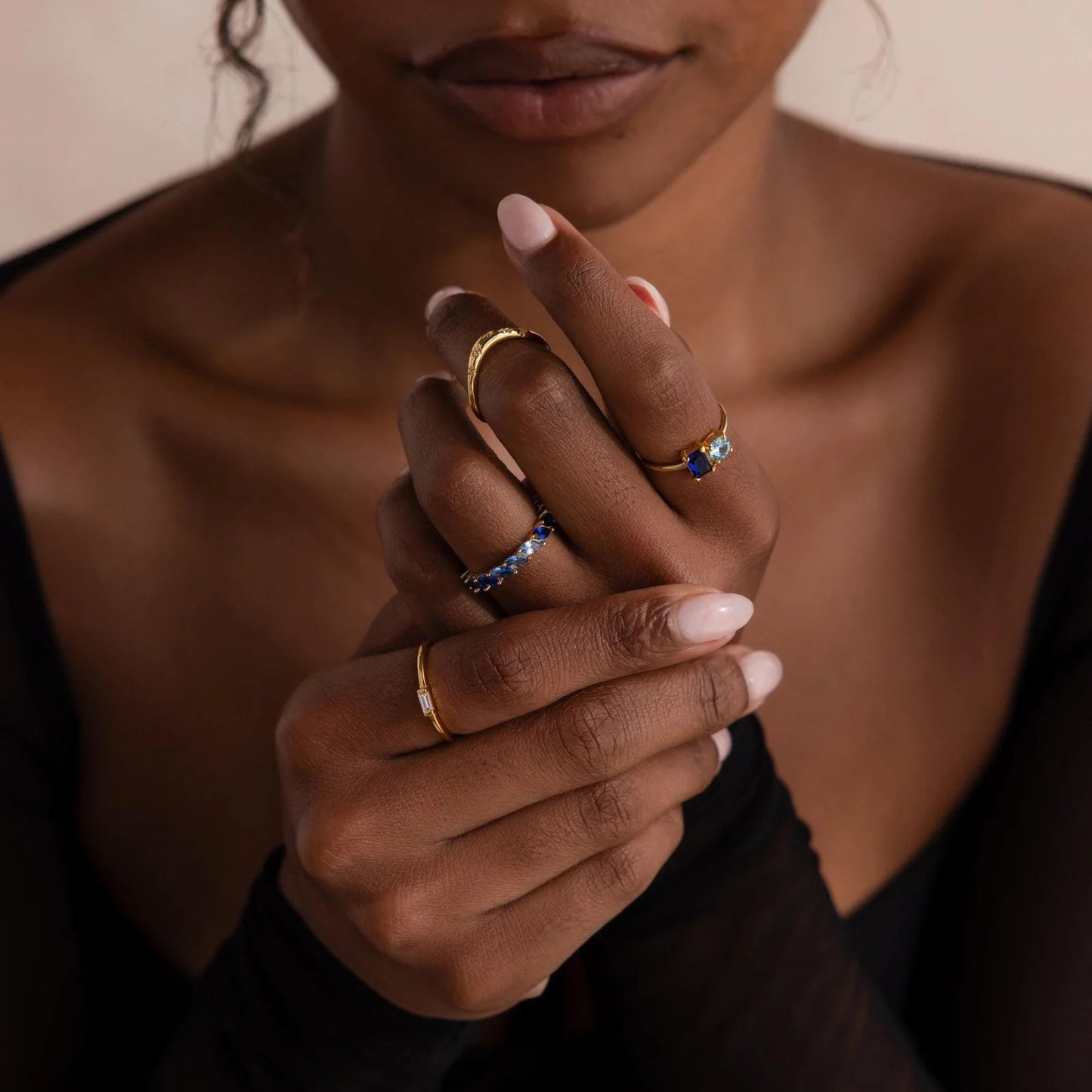 Close-up of a person's hands with multiple rings on a neutral background