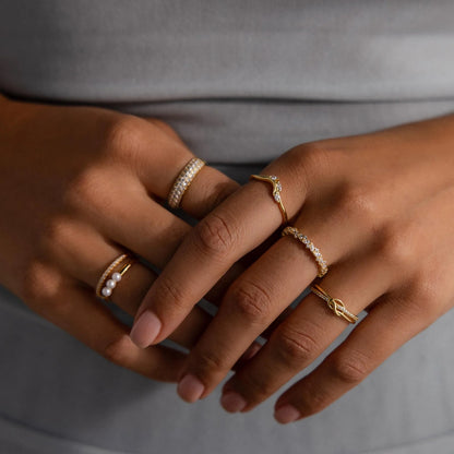 Close-up of a hand wearing multiple gold rings with pearls on a neutral background