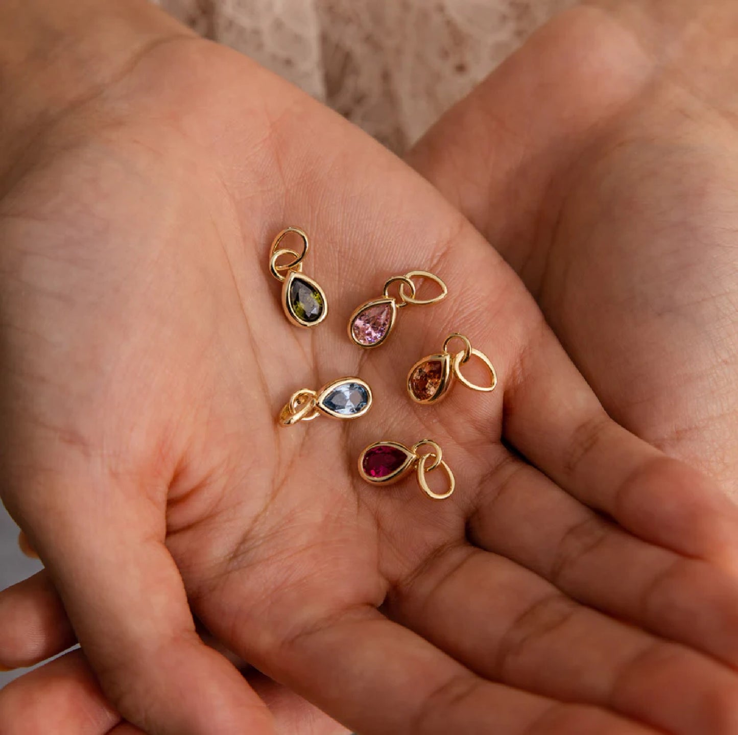 Gold jewelry charms with gemstones held in a hand