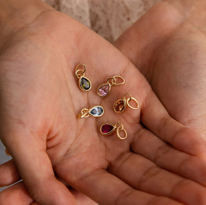 Gold jewelry charms with gemstones held in a hand