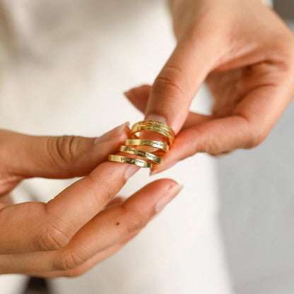 Gold rings being held between fingers with a neutral background