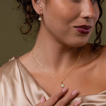 Woman wearing a gold necklace with a pendant against a brown background