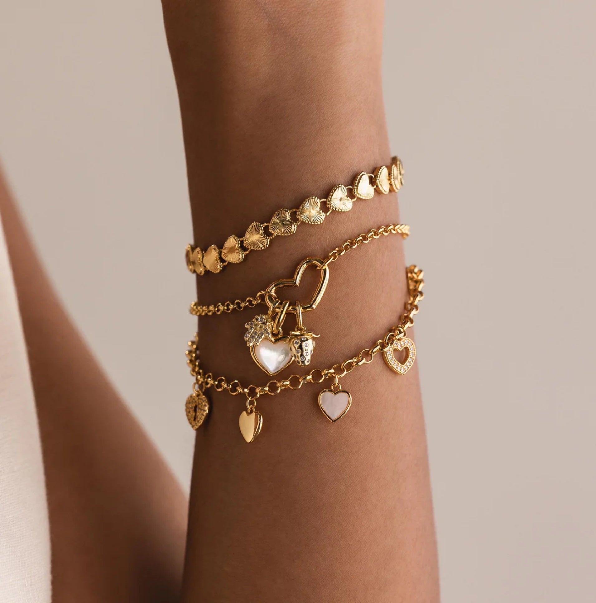Gold bracelets with heart-shaped charms on a wrist against a neutral background