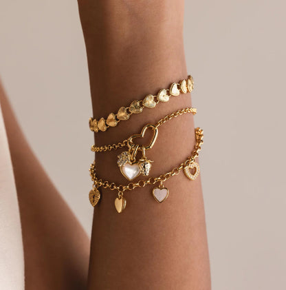 Gold bracelets with heart-shaped charms on a wrist against a neutral background
