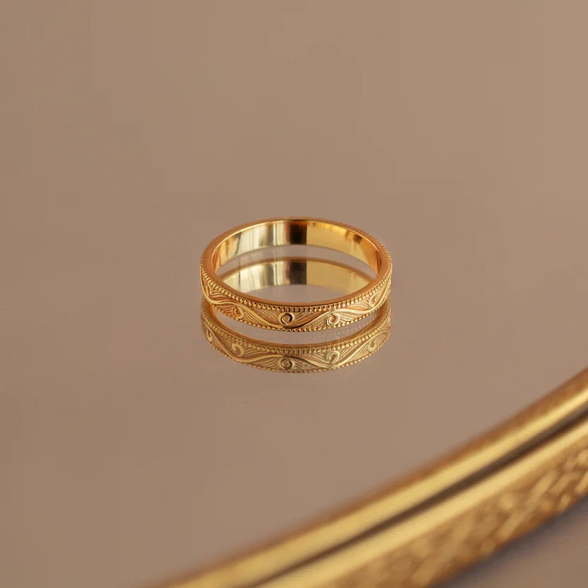 Gold ring with intricate design on a reflective surface
