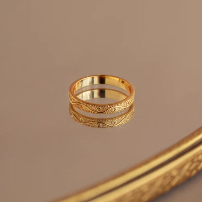 Gold ring with intricate design on a reflective surface