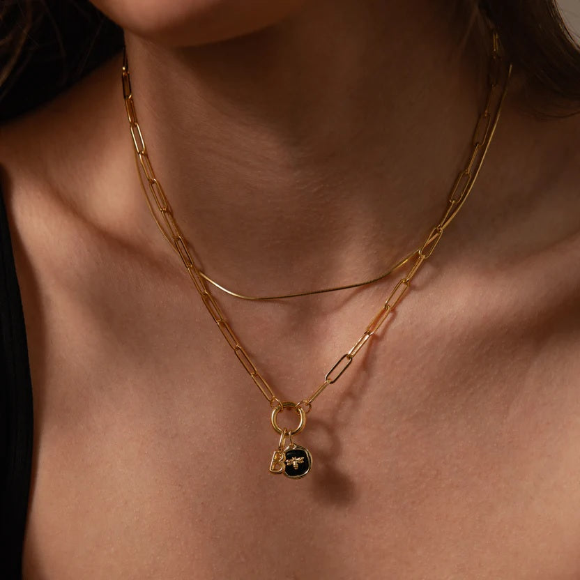 Close-up of a person wearing a gold necklace with a pendant on a neutral background