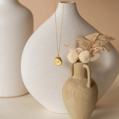 Necklace with pendant hanging over a vase with dried flowers against a beige background