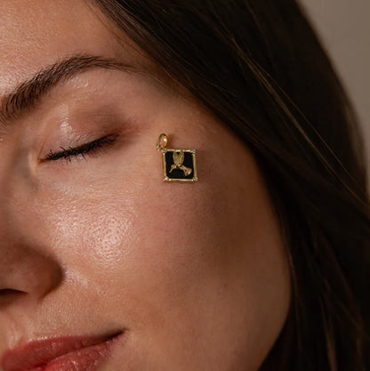 Close-up of a woman's face with a gold earring featuring a black pendant.