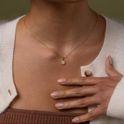 Person wearing a gold necklace with a diamond pendant, hand resting on chest.