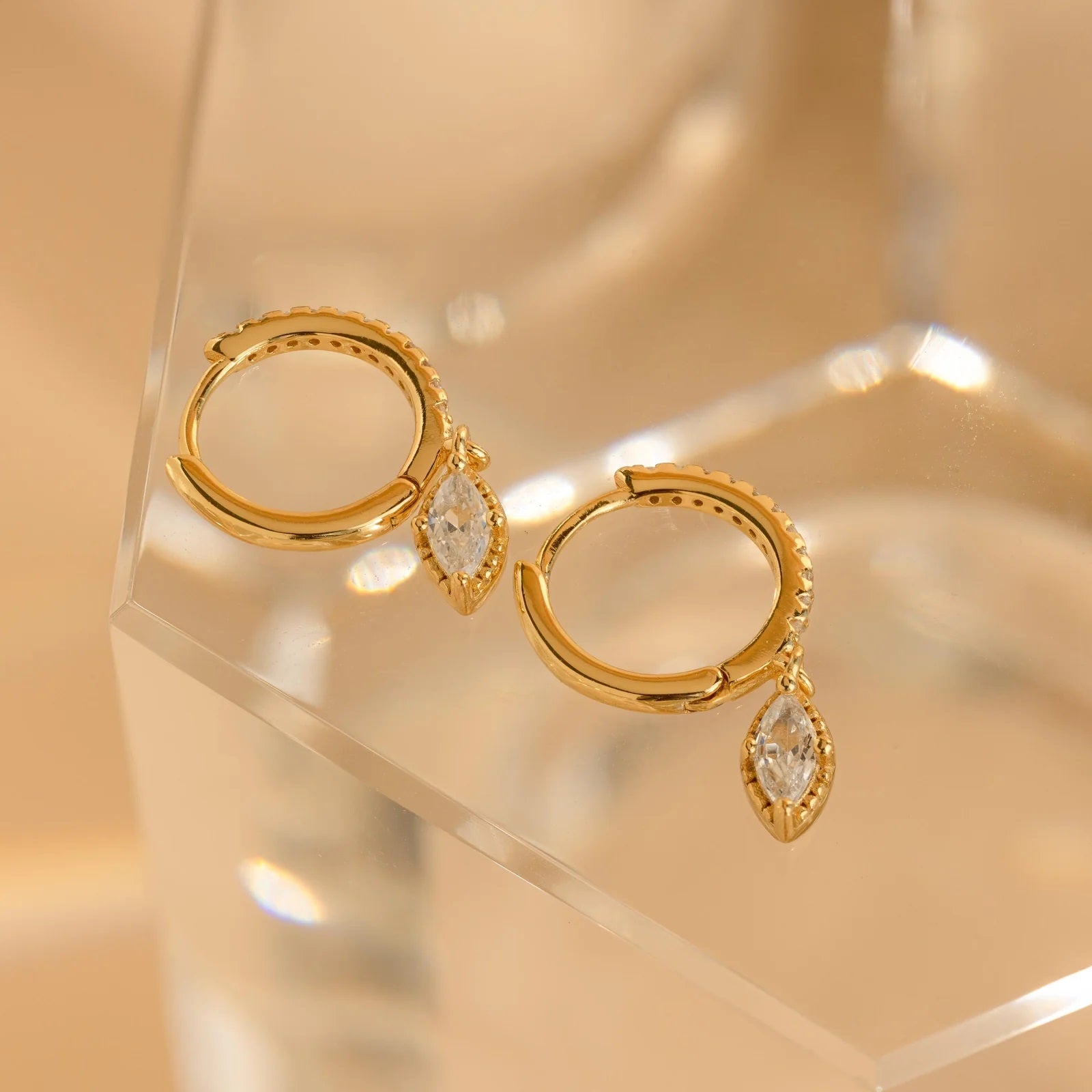 Gold hoop earrings with teardrop-shaped gemstones on a clear stand.