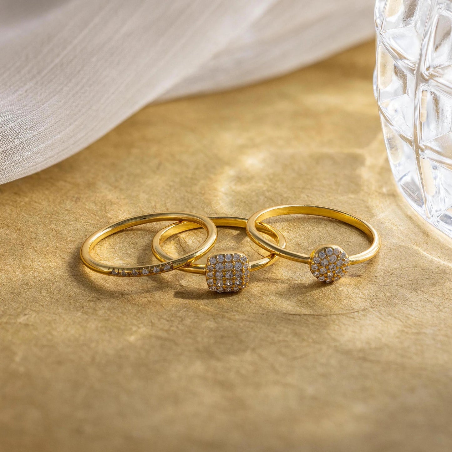 Three gold rings with gemstones on a beige surface