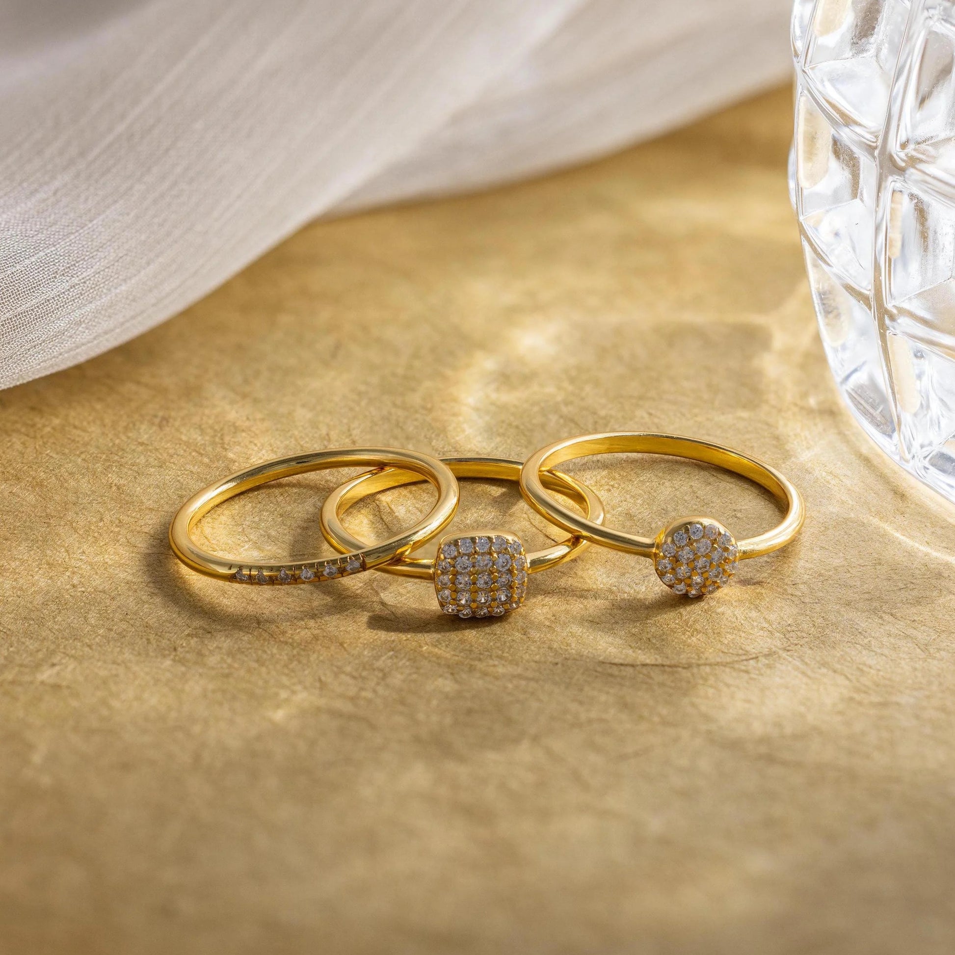 Three gold rings with gemstones on a beige surface