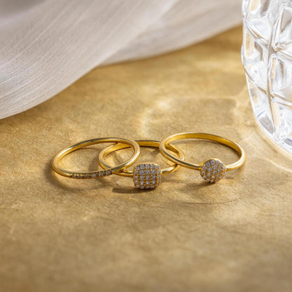 Three gold rings with gemstones on a beige surface