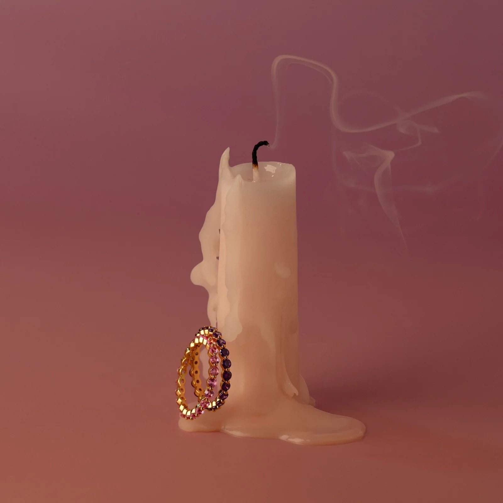 Candle with a decorative earring on a pink background