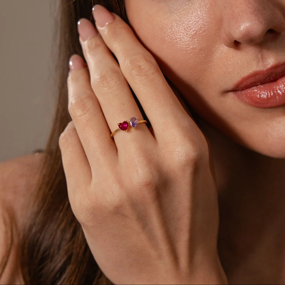 Close-up of a woman wearing a ring with rubies on a neutral background