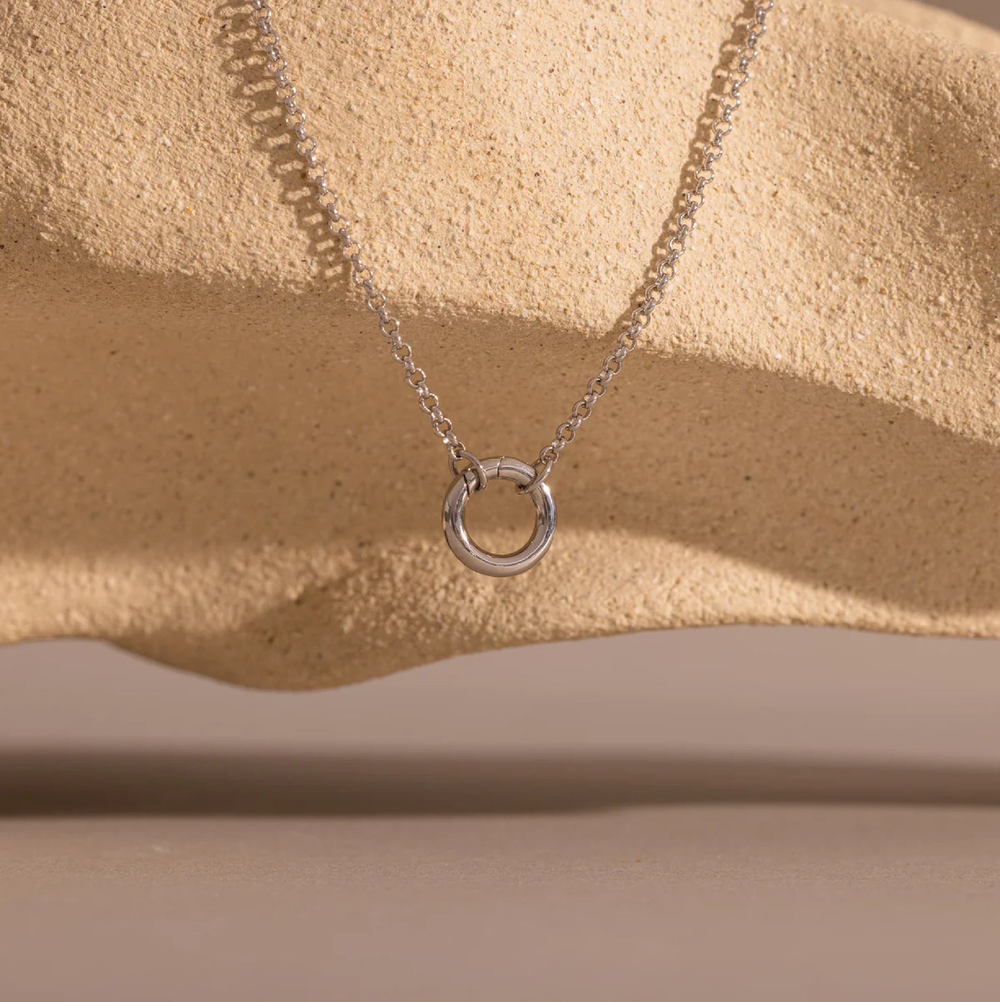 Silver necklace with a circular pendant on a beige surface