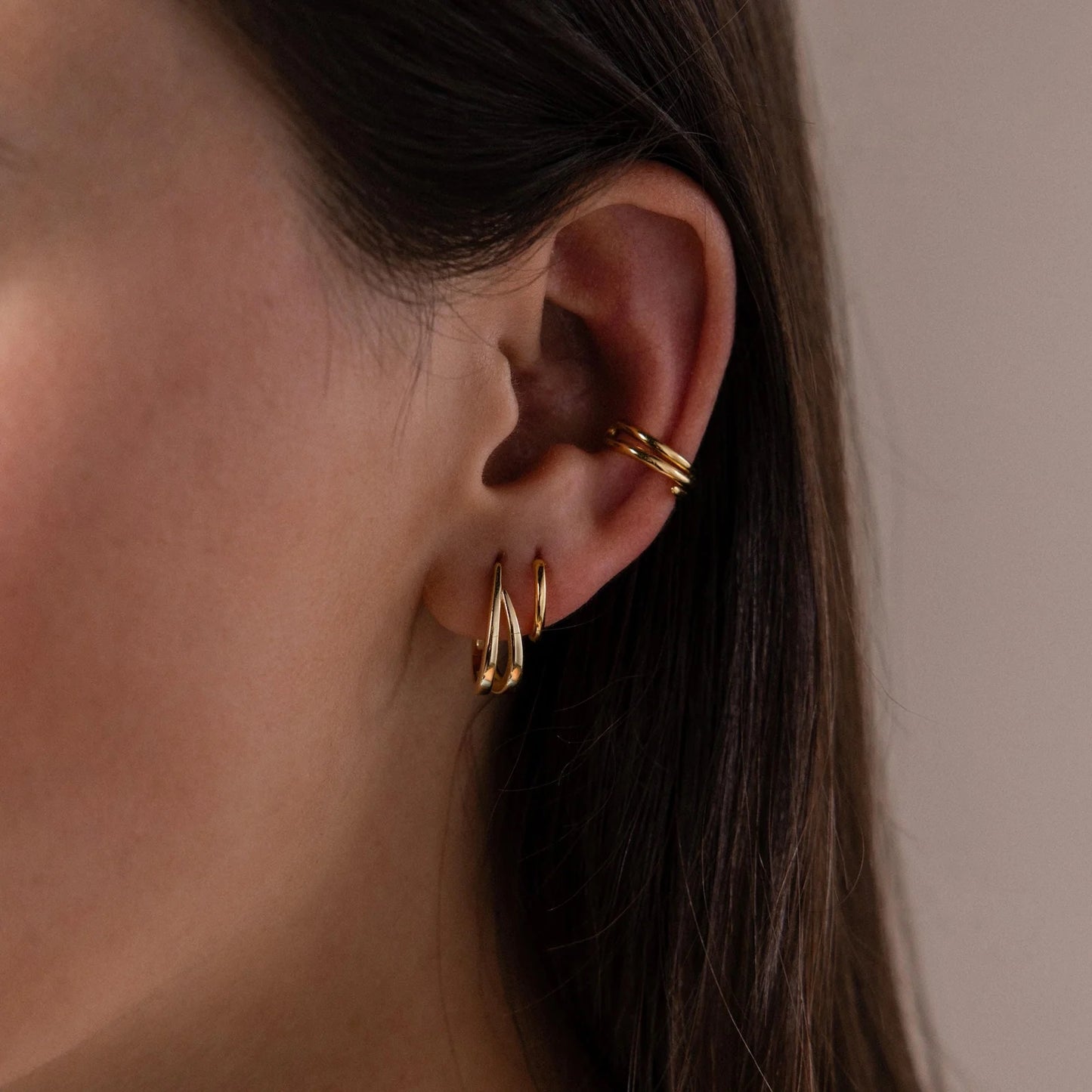 Close-up of a person wearing gold earrings and a gold hoop earring.