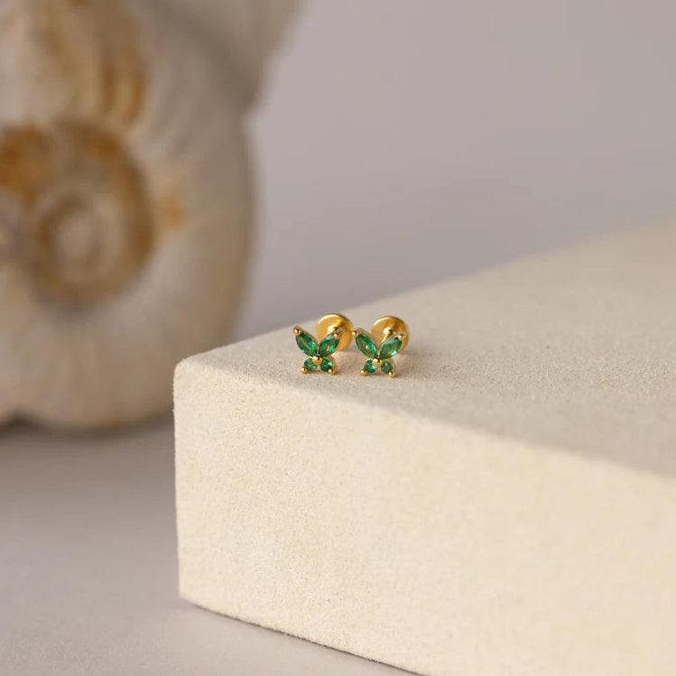 Gold butterfly earrings with green gemstones on a beige jewelry box.