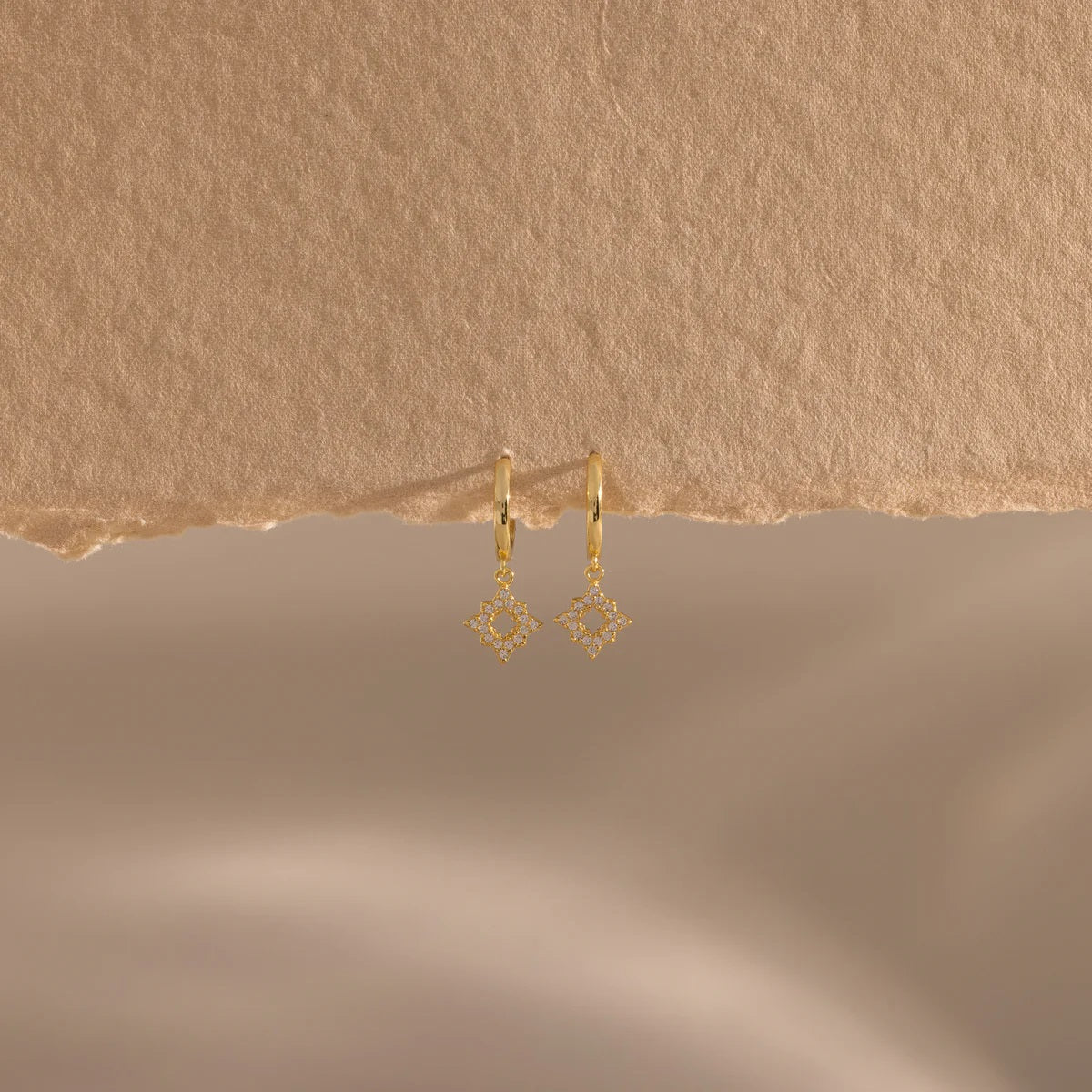 Gold earrings on a textured beige background