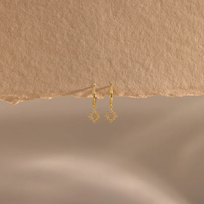 Gold earrings on a textured beige background