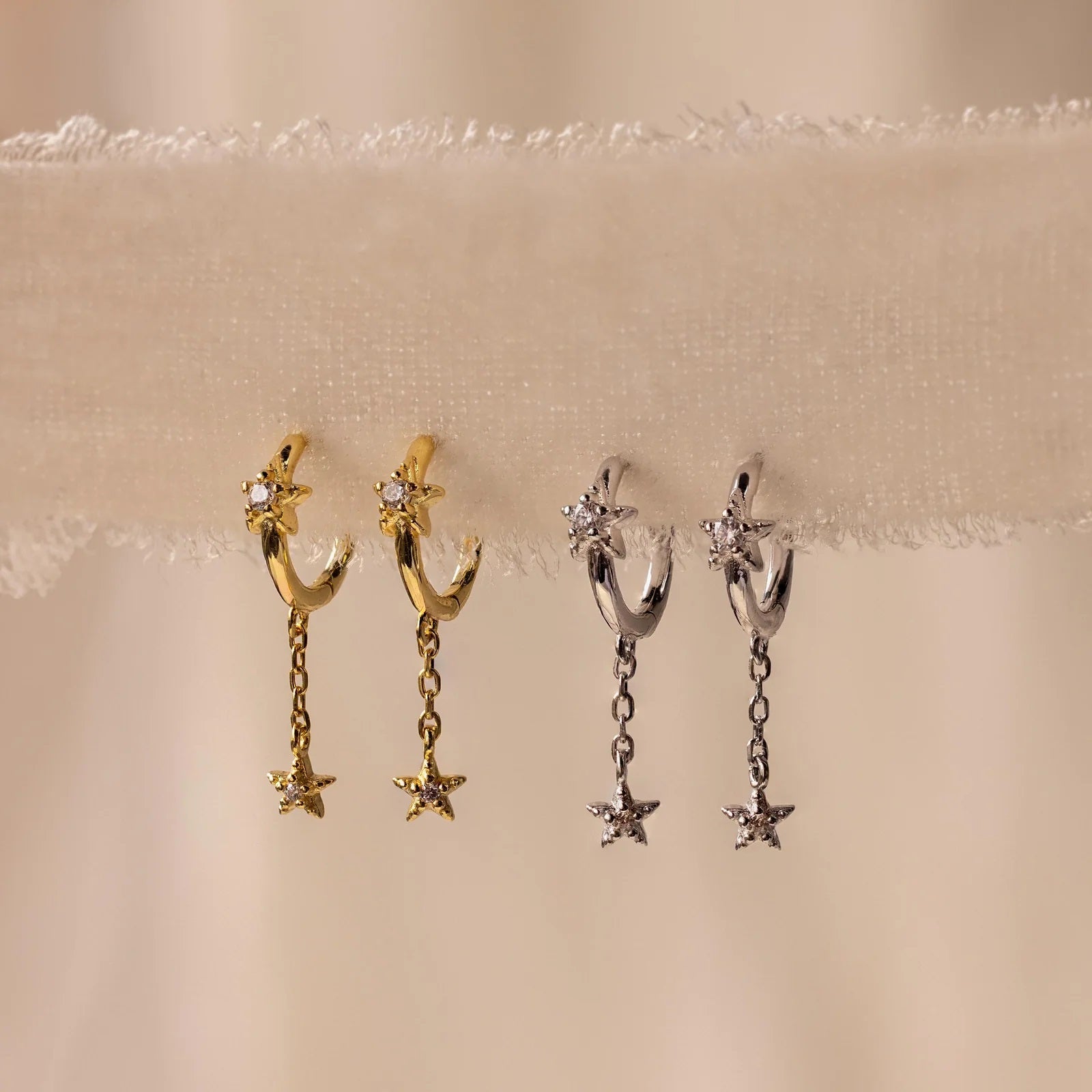 Pair of gold and silver hoop earrings with star-shaped pendants on a beige background