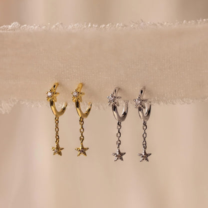Pair of gold and silver hoop earrings with star-shaped pendants on a beige background