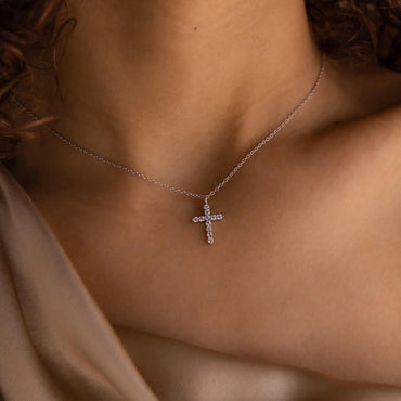 Silver cross necklace on a person's neck with a neutral background