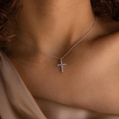 Silver cross necklace on a person's neck with a neutral background