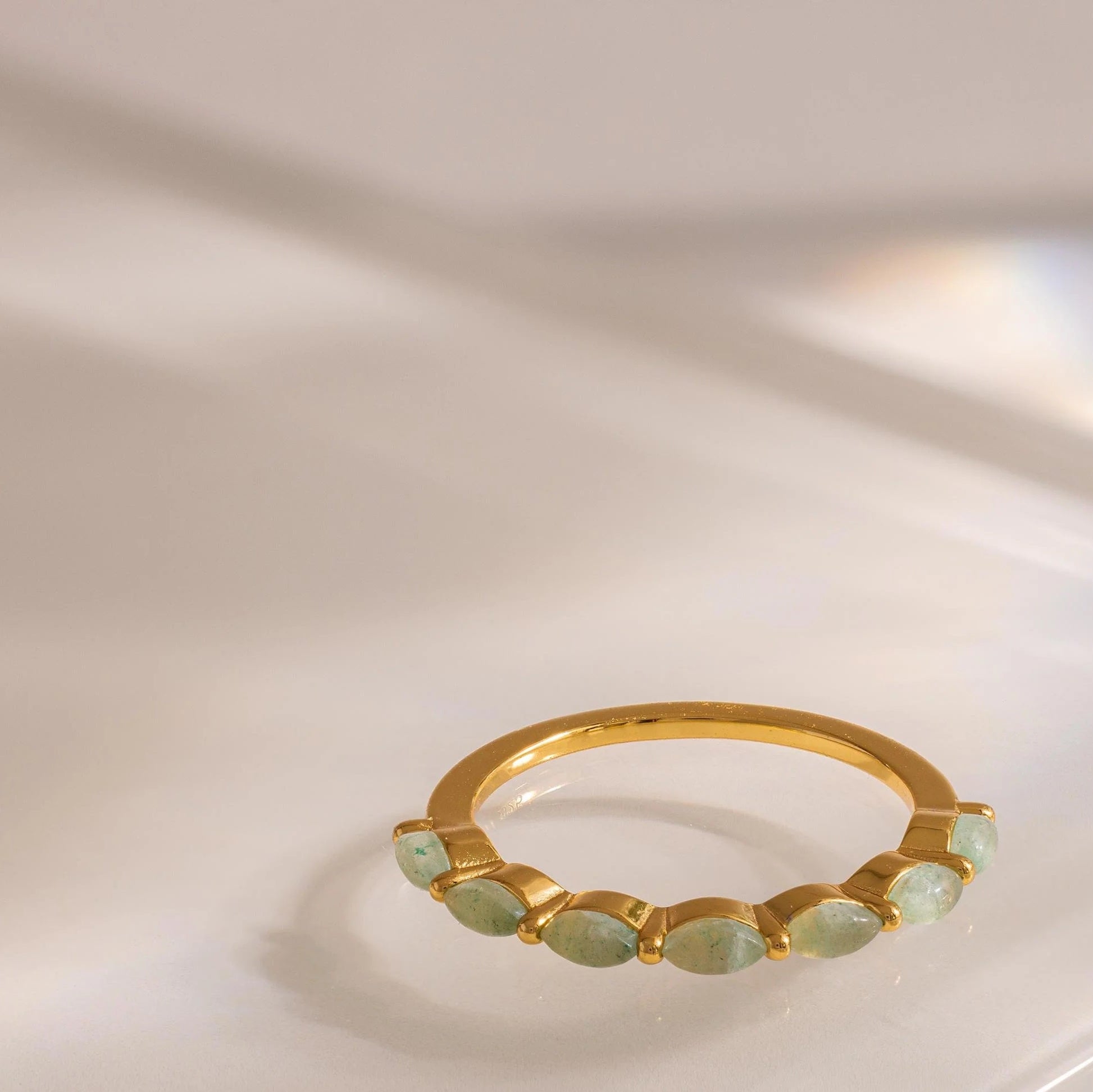 Gold ring with green gemstones on a reflective surface
