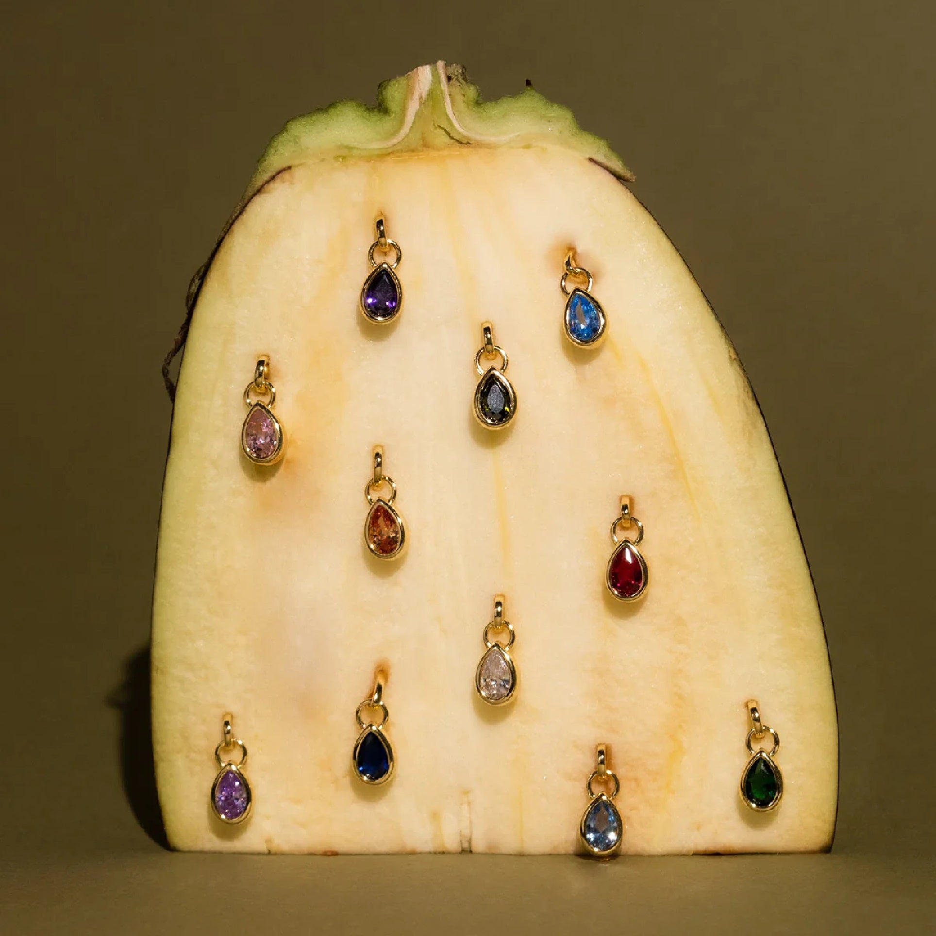 Gold teardrop-shaped jewelry on a halved white eggplant against a brown background