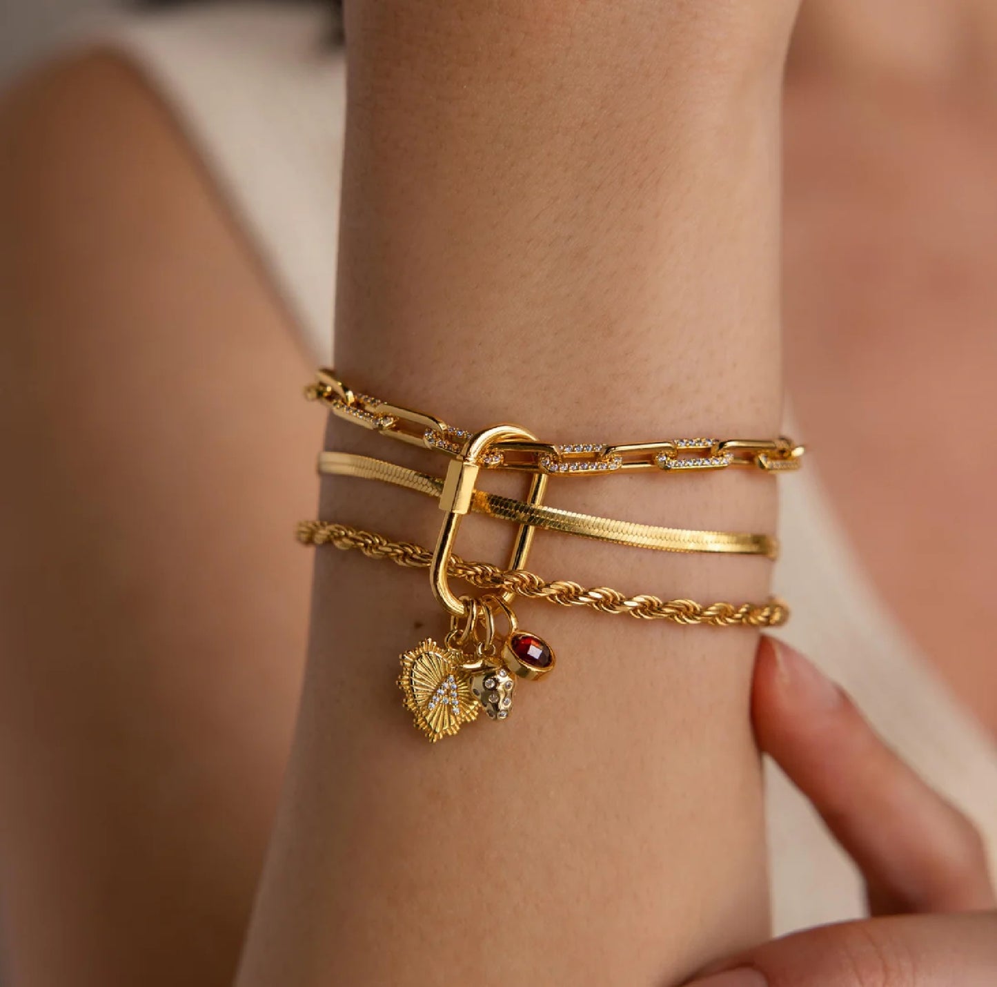 Gold bracelets with charms on a wrist against a neutral background