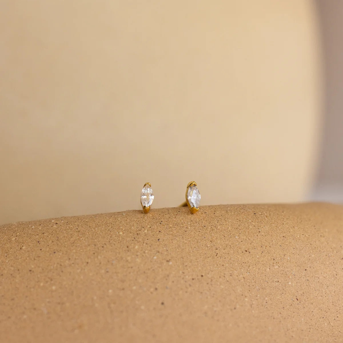 Gold earrings with clear gemstones on a beige surface