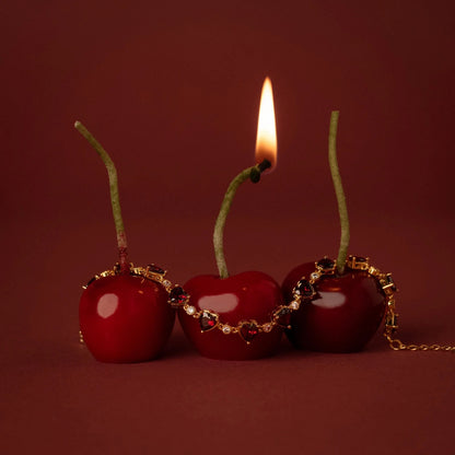 Three cherries with gold chains and a lit candle on a red background