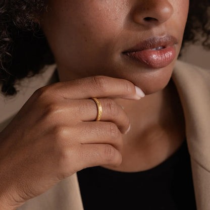 Close-up of a person wearing a gold ring with a neutral background