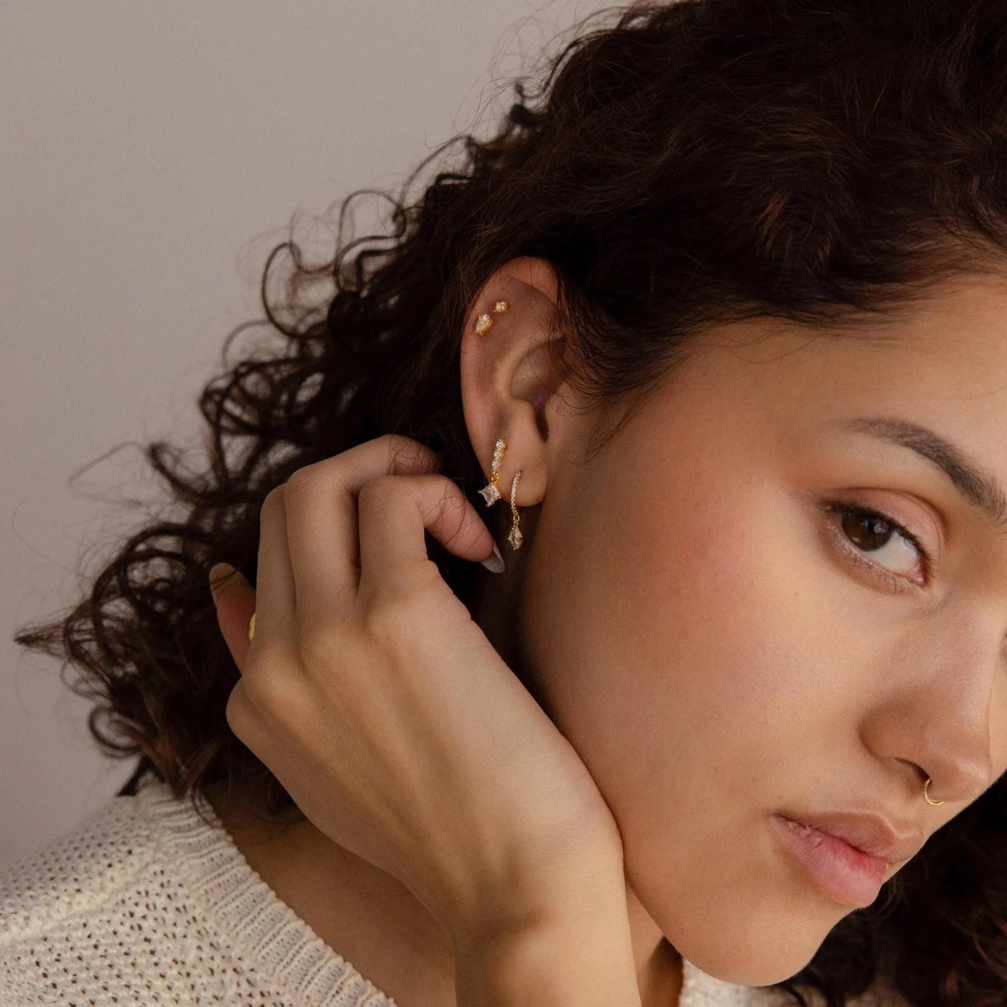 Close-up of a woman adjusting an earring with a neutral background