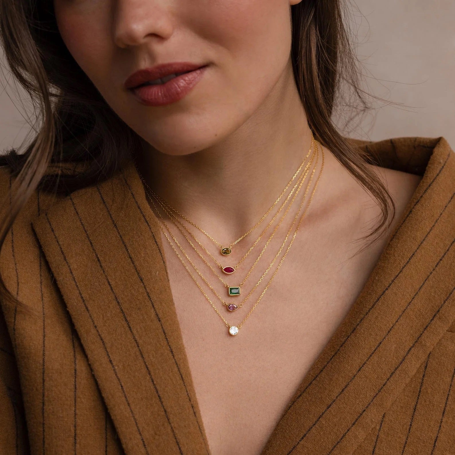 Close-up of a woman wearing a gold necklace with gemstones against a neutral background