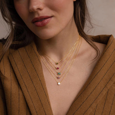 Close-up of a woman wearing a gold necklace with gemstones against a neutral background