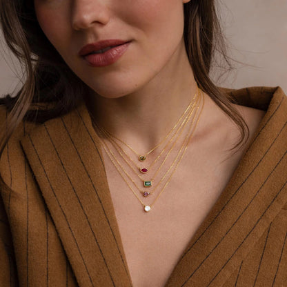 Close-up of a woman wearing a gold necklace with gemstones against a neutral background
