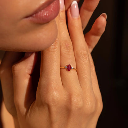 Close-up of a hand wearing a ring with a red gemstone, holding the face.
