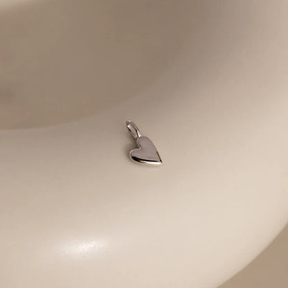 Heart-shaped silver pendant on a beige background