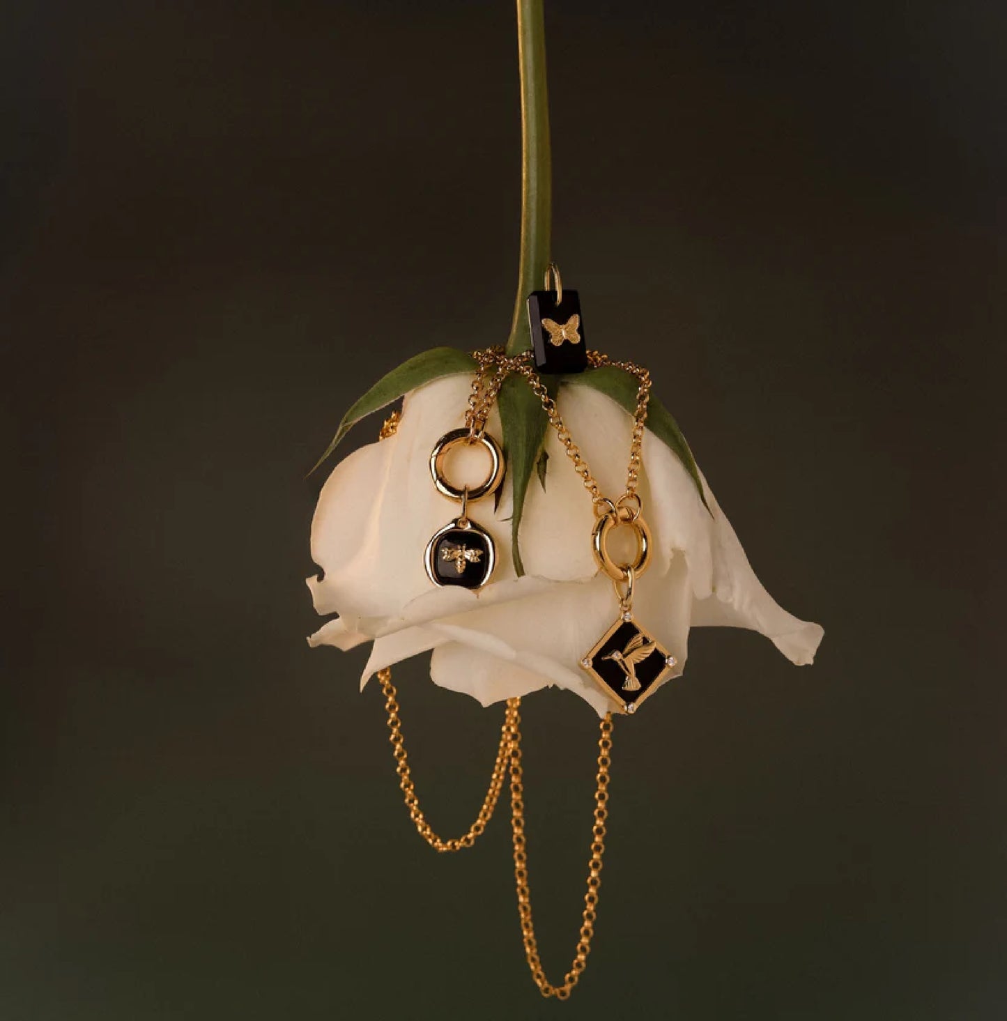 Gold necklaces with black pendants on a white rose against a dark background