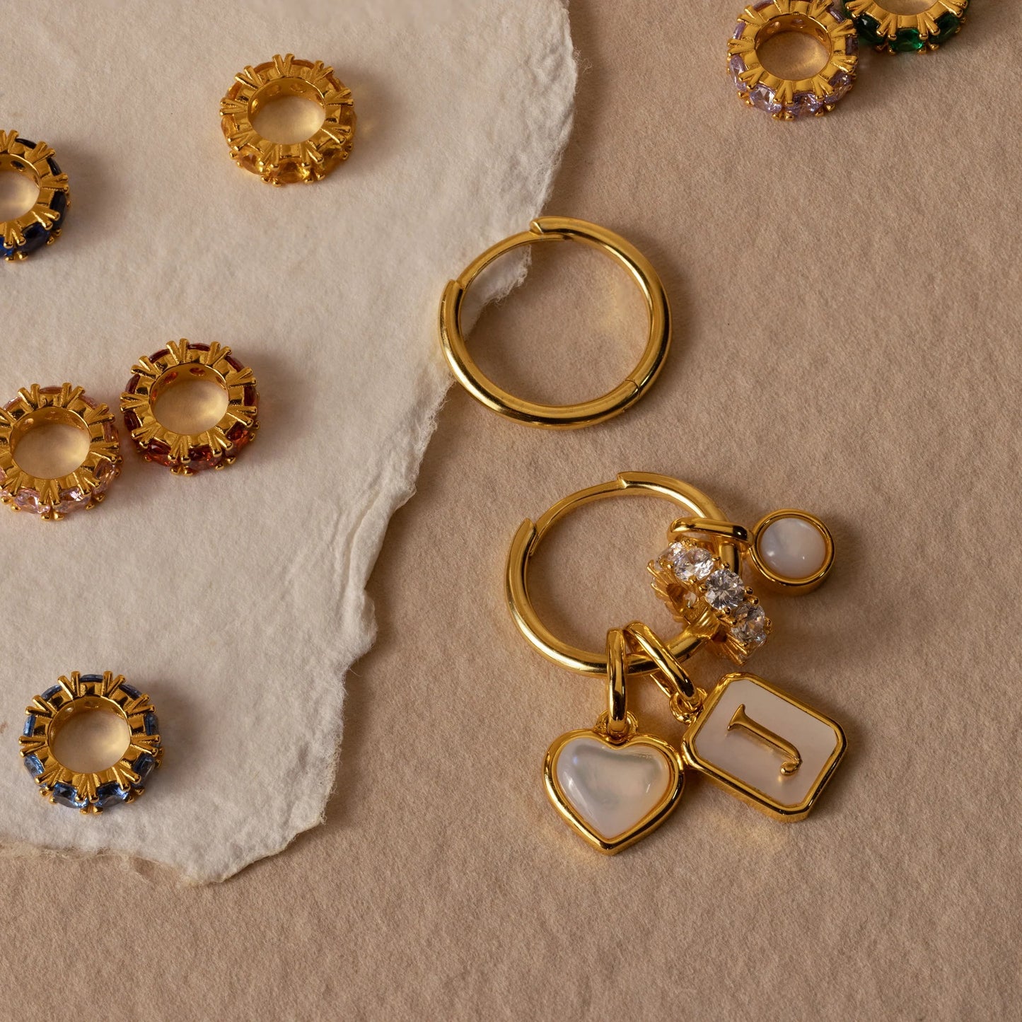 Gold hoop earrings with charms on a beige stone surface