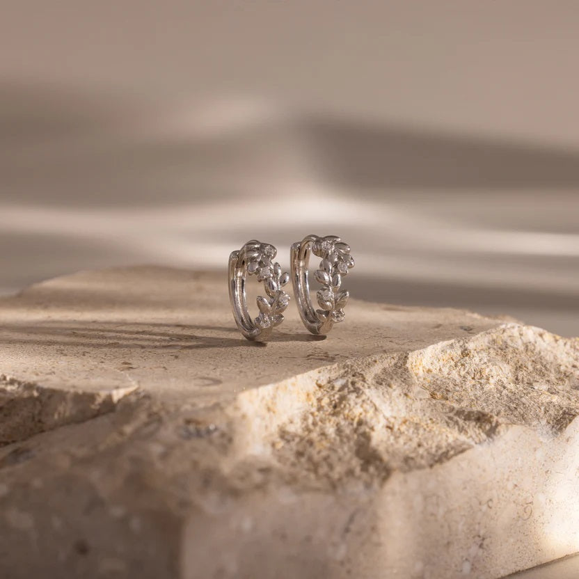 Silver hoop earrings on a textured stone surface with a blurred natural background