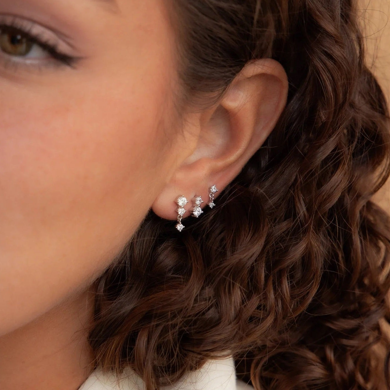 Close-up of a woman's ear wearing a set of earrings with a neutral background